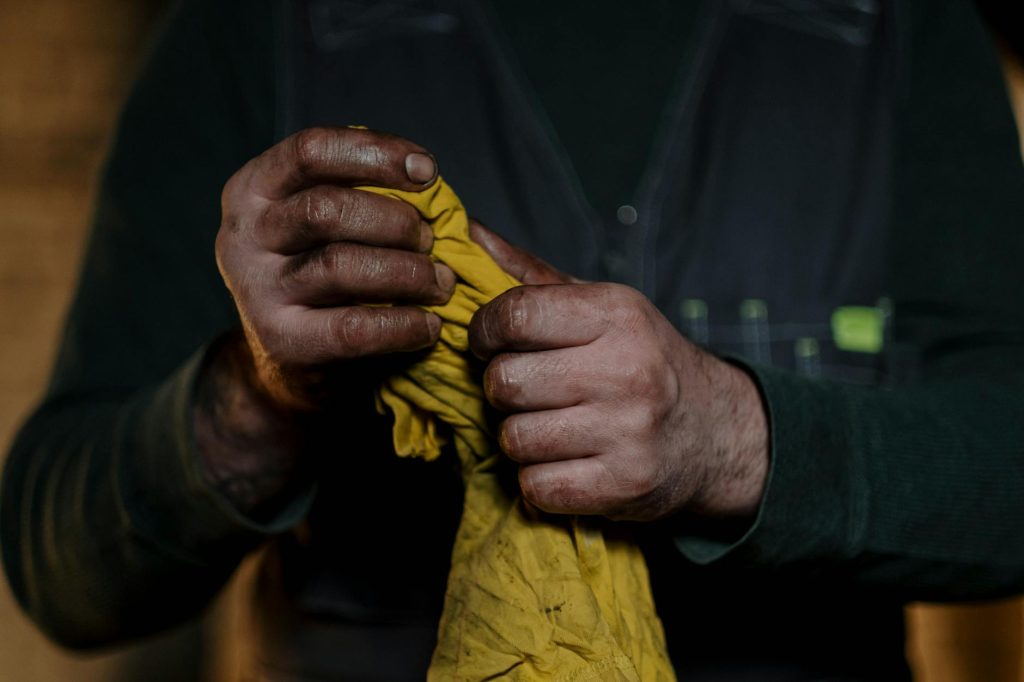 Detailed shot of rugged hands gripping a yellow cloth, emphasizing manual labor.