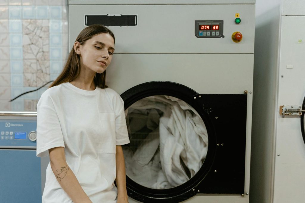 A woman in a laundry facility standing by a washing machine, contemplating the process.
