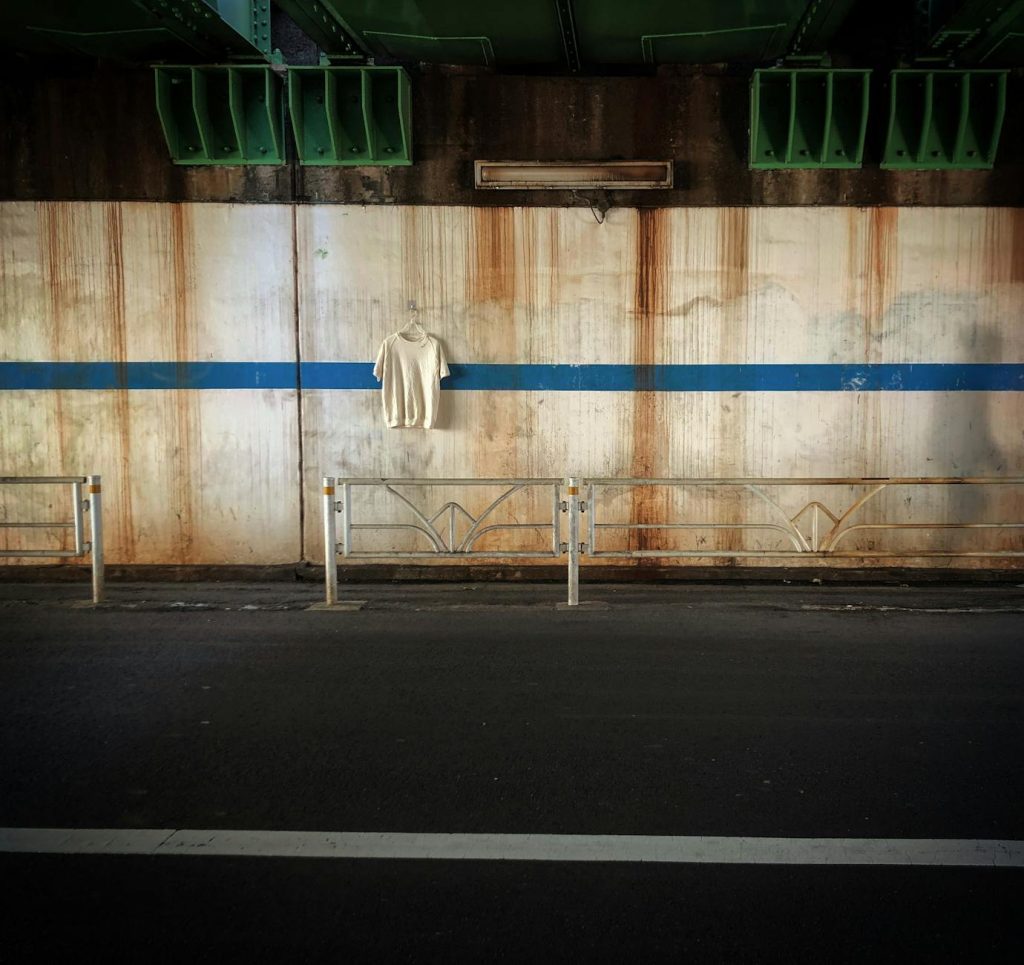 A lone white t-shirt hangs on a rusty wall in Shibuya City under a bridge. Urban decay captures the eye.