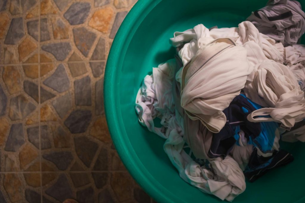 Top view of a laundry basket filled with crumpled clothes on a tiled floor.