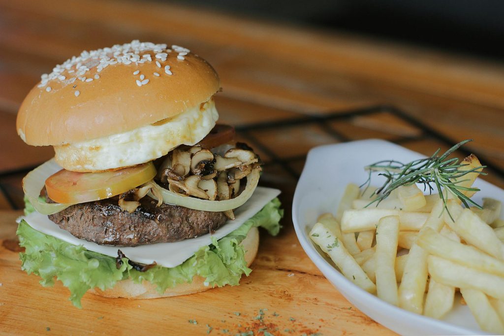 A delicious gourmet burger with mushroom topping and fries served on a wooden table.