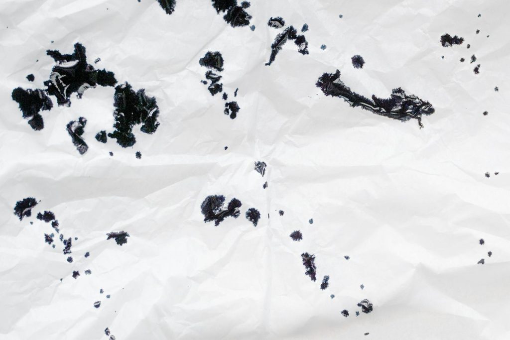 Crumpled white paper with scattered black ink spots creating an abstract pattern.