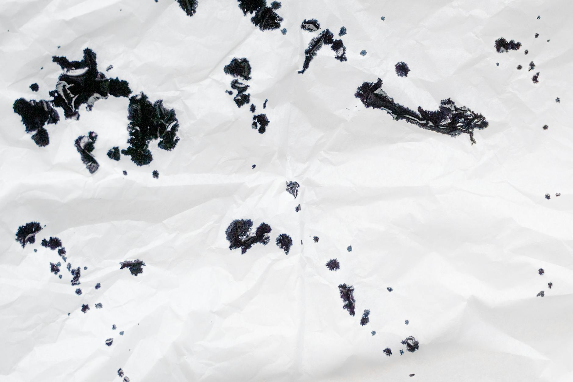 Crumpled white paper with scattered black ink spots creating an abstract pattern.