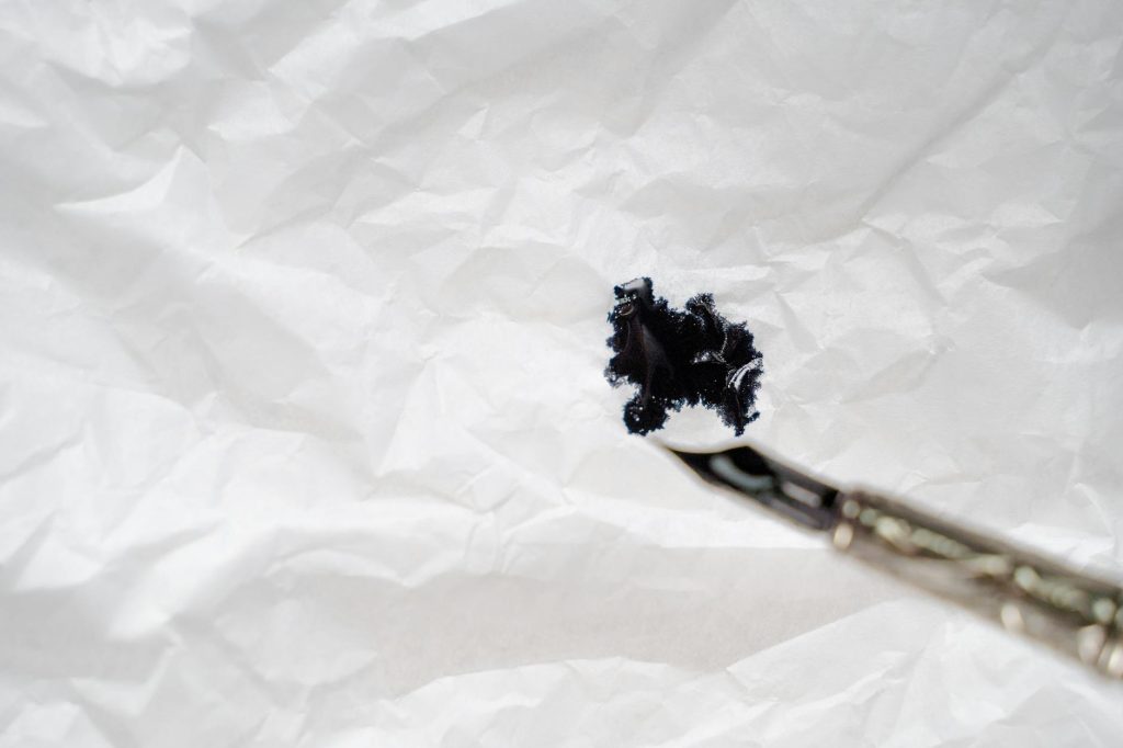 Close-up of a black ink splash on wrinkled white paper with a brush.