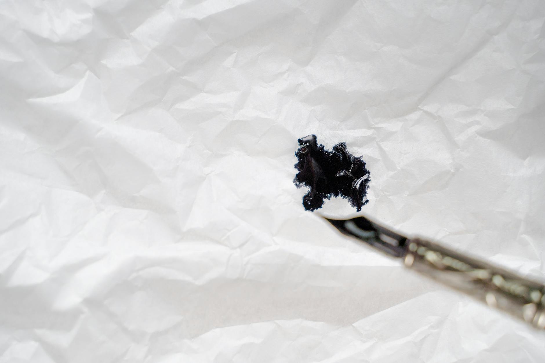 Close-up of a black ink splash on wrinkled white paper with a brush.