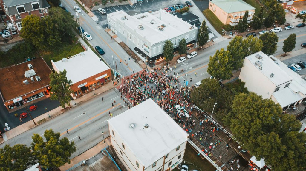 Aerial view of unrecognizable people on asphalt roadway near houses and trees in town in demonstration