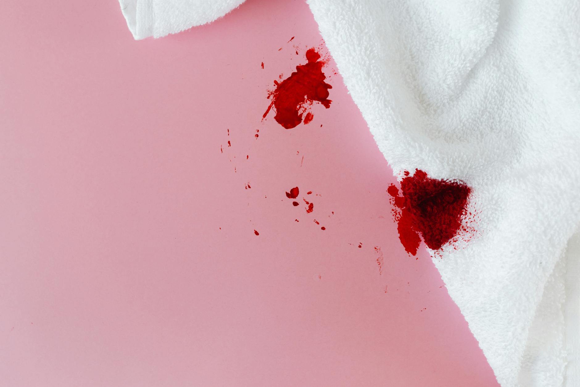 White towel with red blood stains on pink surface, showing menstrual concept.