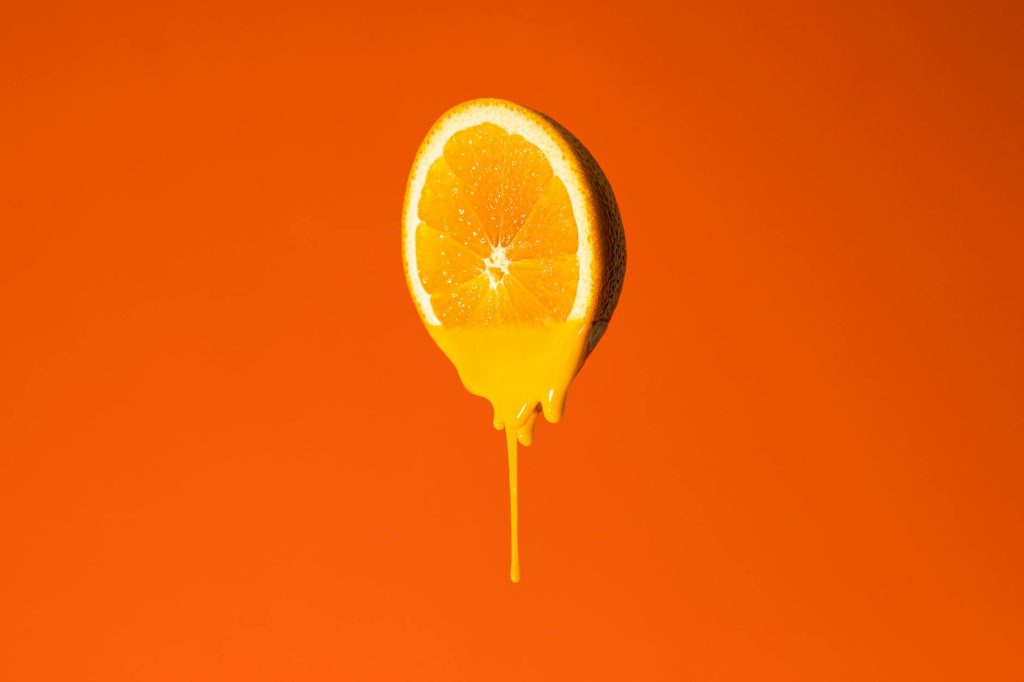A fresh orange slice dripping juice against a vibrant orange background.