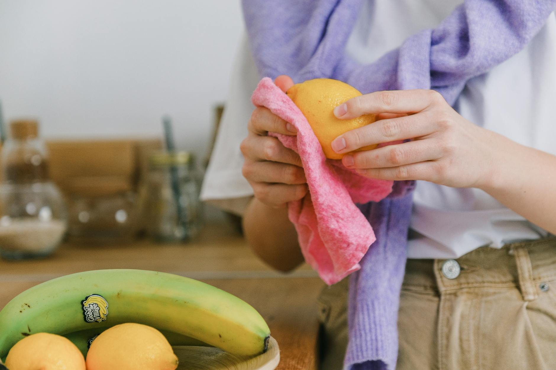Close-up of a woman wiping a lemon with a cloth in a kitchen setting.