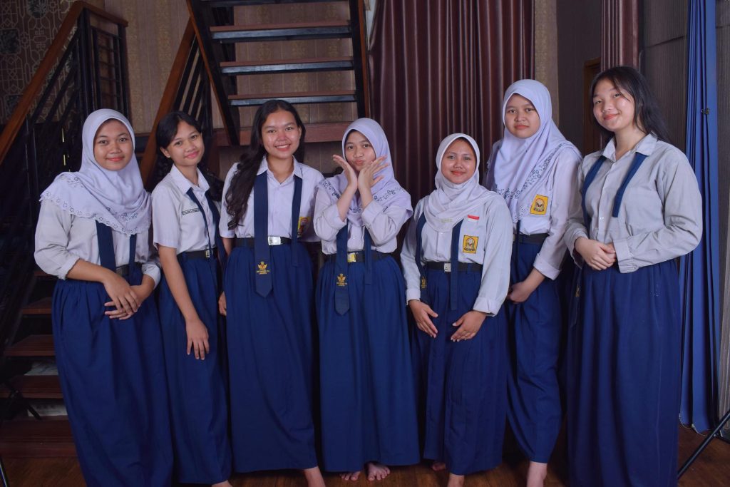 Seven teenagers in school uniforms posing happily indoors, showcasing friendship.