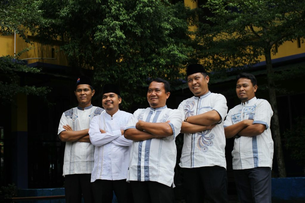 Five Indonesian men in traditional attire pose outdoors, showcasing cultural fashion.