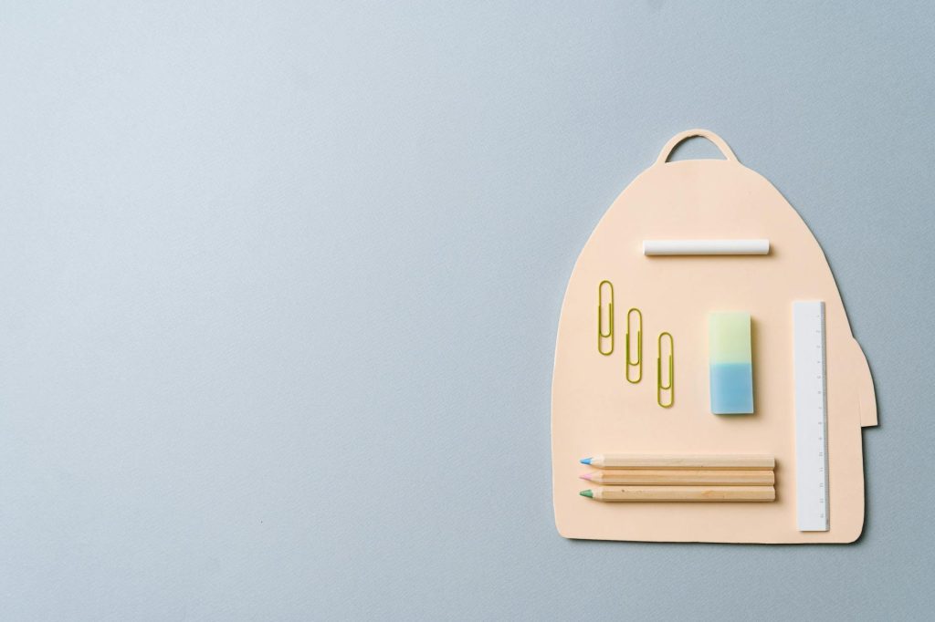 Minimalist top view of school supplies creatively arranged on a backpack-shaped platform.