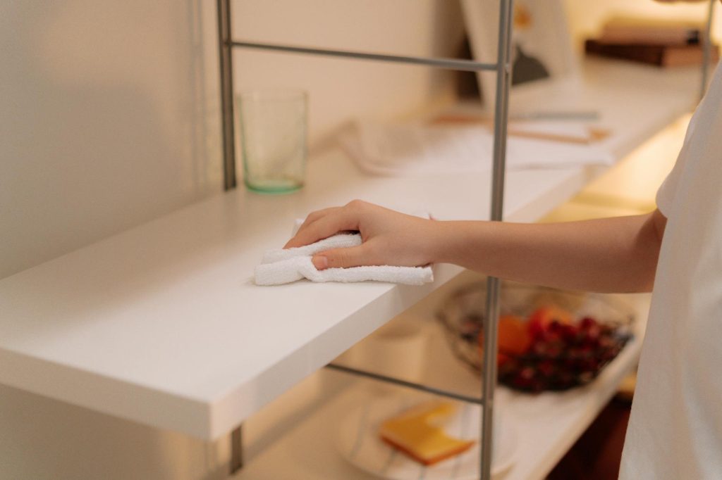 A person cleans a white shelf with a cloth, focusing on home maintenance.