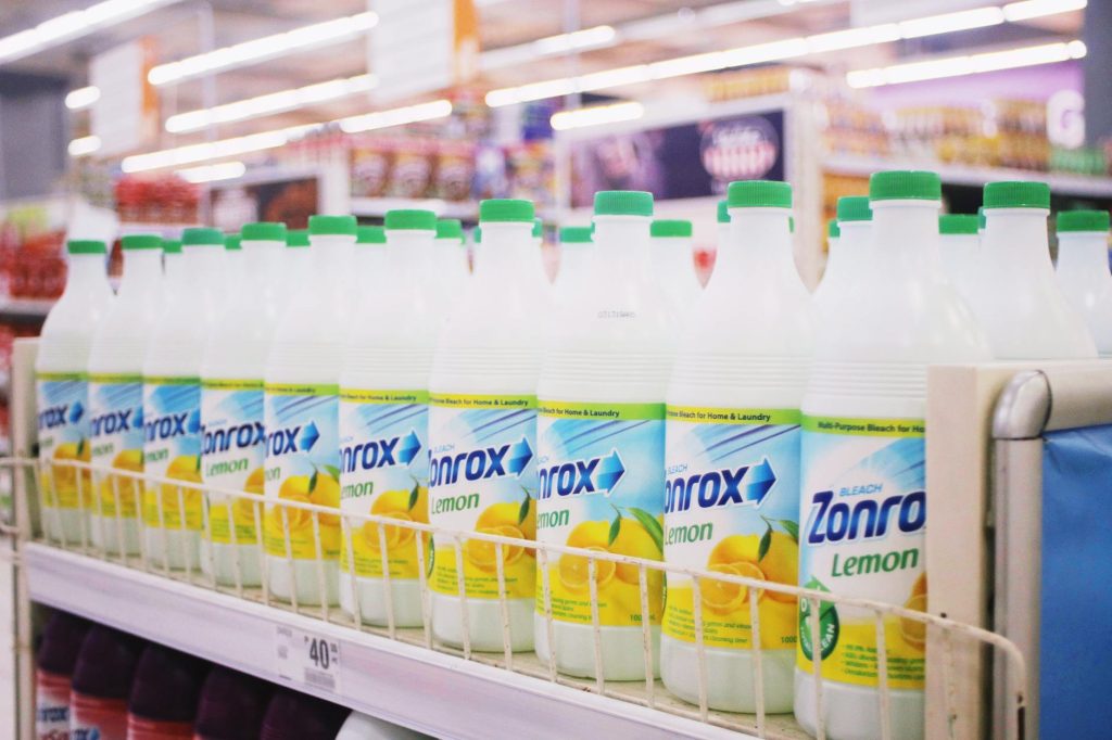 Rows of plastic bottles of bleach with smell of lemon placed on shelves in supermarket