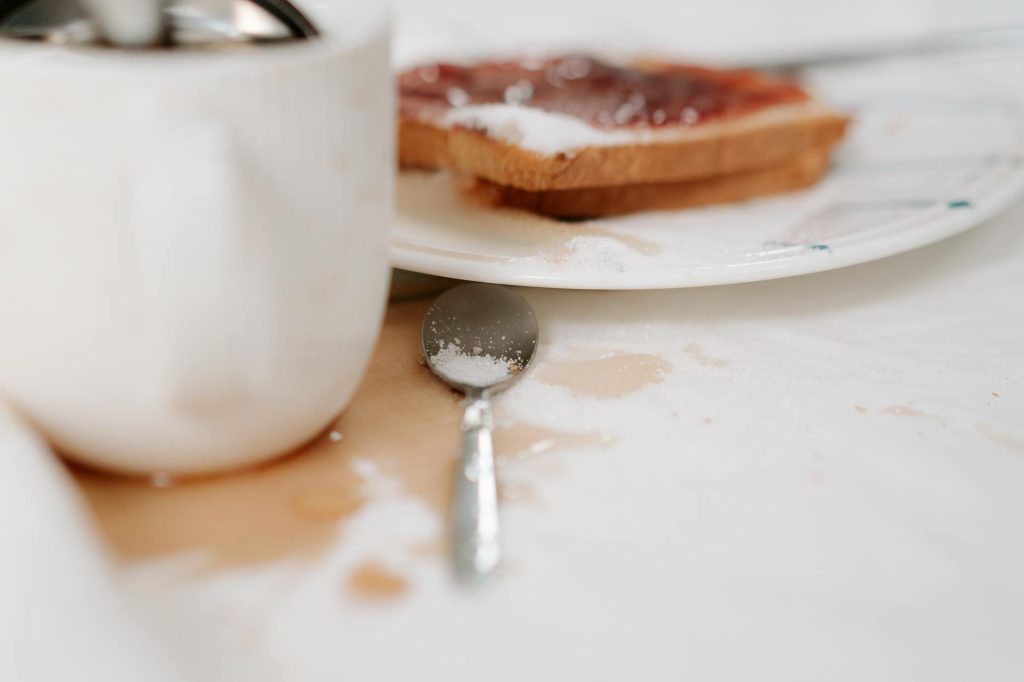 Close-up of a messy breakfast table with coffee spill, toast, and sugar.