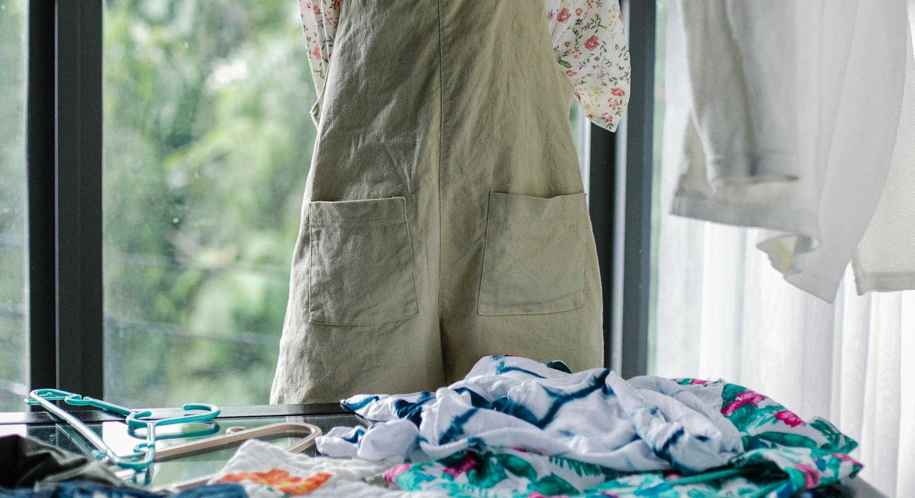 Crop anonymous woman in casual wear sorting and picking garments from clothes heaped on table in light cloakroom