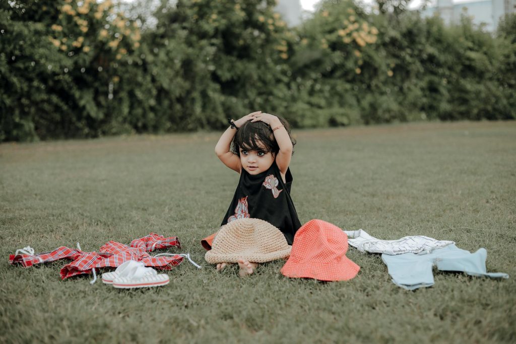 A cute child playing with hats on a grassy lawn in Surat, India. Perfect for playful outdoor moments.