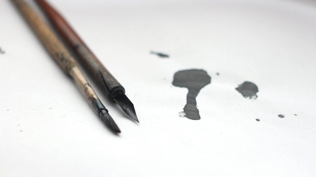 Close-up of calligraphy tools and ink spill on white surface, perfect for artistic themes.