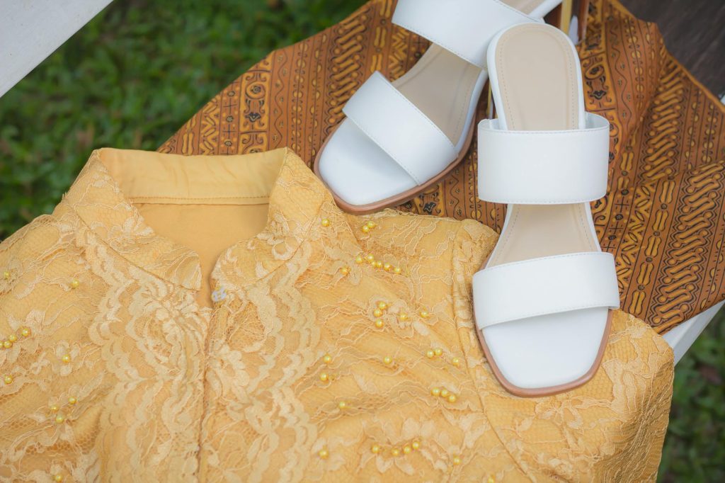 Close-up of an Indonesian kebaya and batik cloth with white sandals.